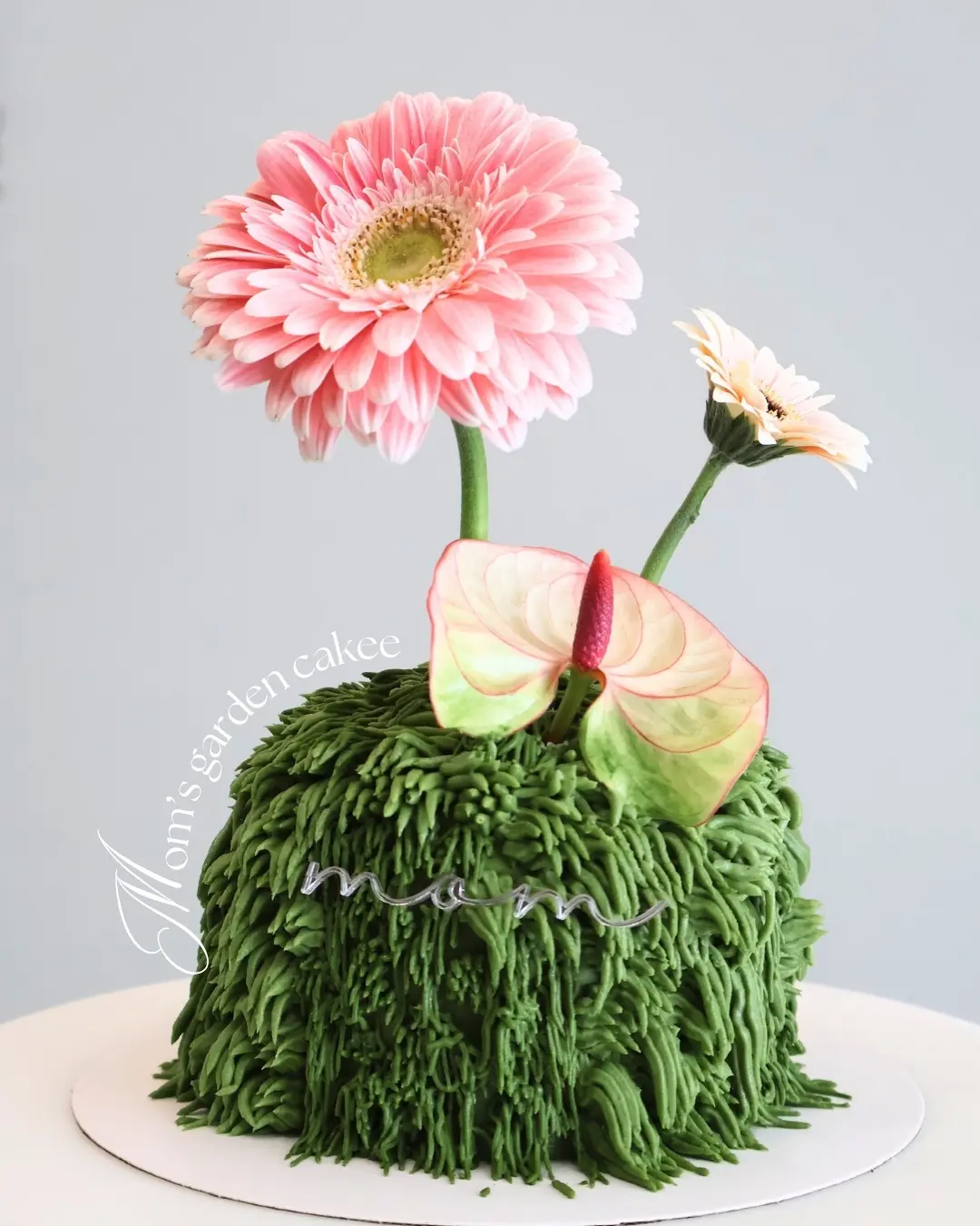 Pastel personalizado decorado como una montaña verde con flores, diseño exclusivo de Bake Me Up
